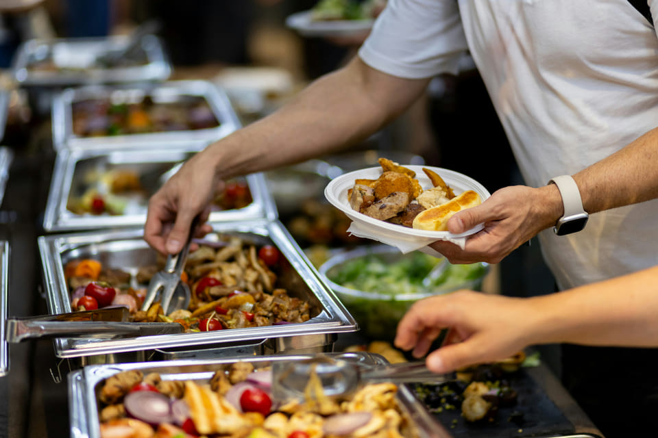 People at a buffet, a person serving themselves while others choose side salads.